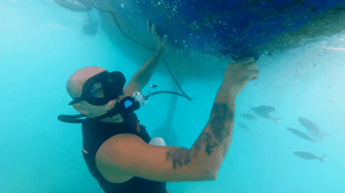 Man cleaning bottom of boat hull using a tankless dive system and scraper