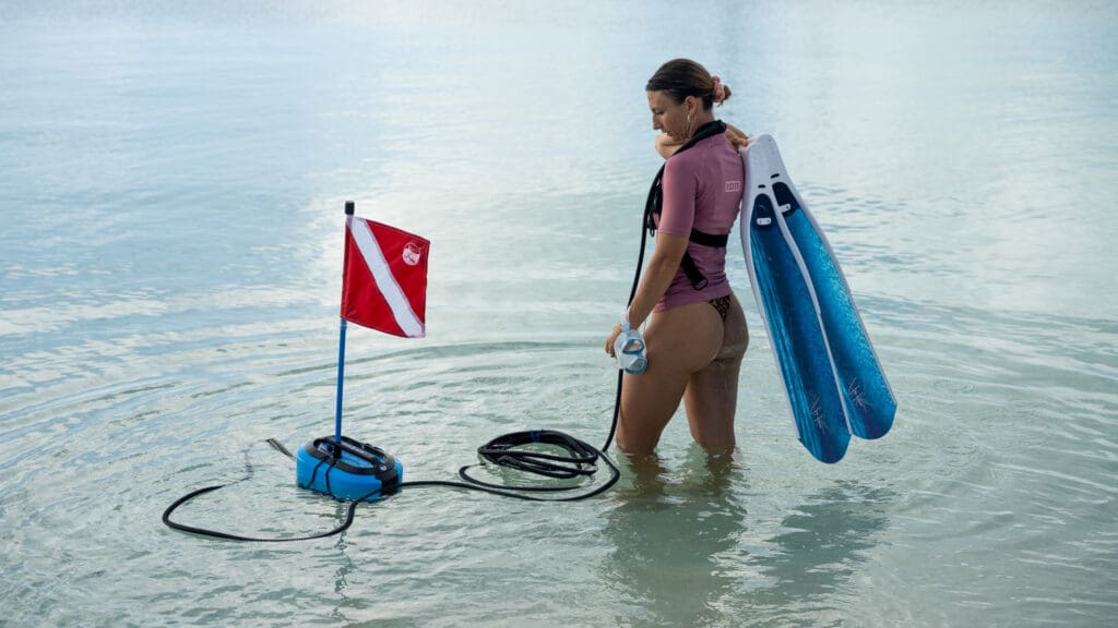 woman-preparing-to-dive-with-blu3-nomad A woman standing in shallow water holding blue fins and a dive mask, with the BLU3 Nomad system.