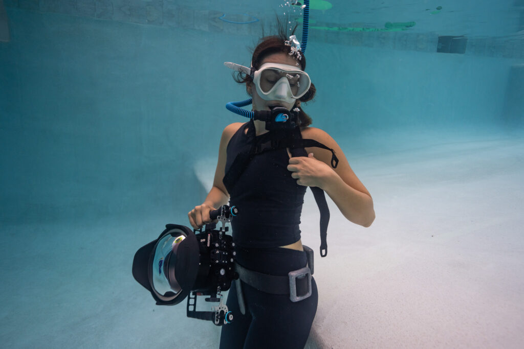 Underwater photographer using BLU3 dive system to breathe, with camera in hand, in a pool.