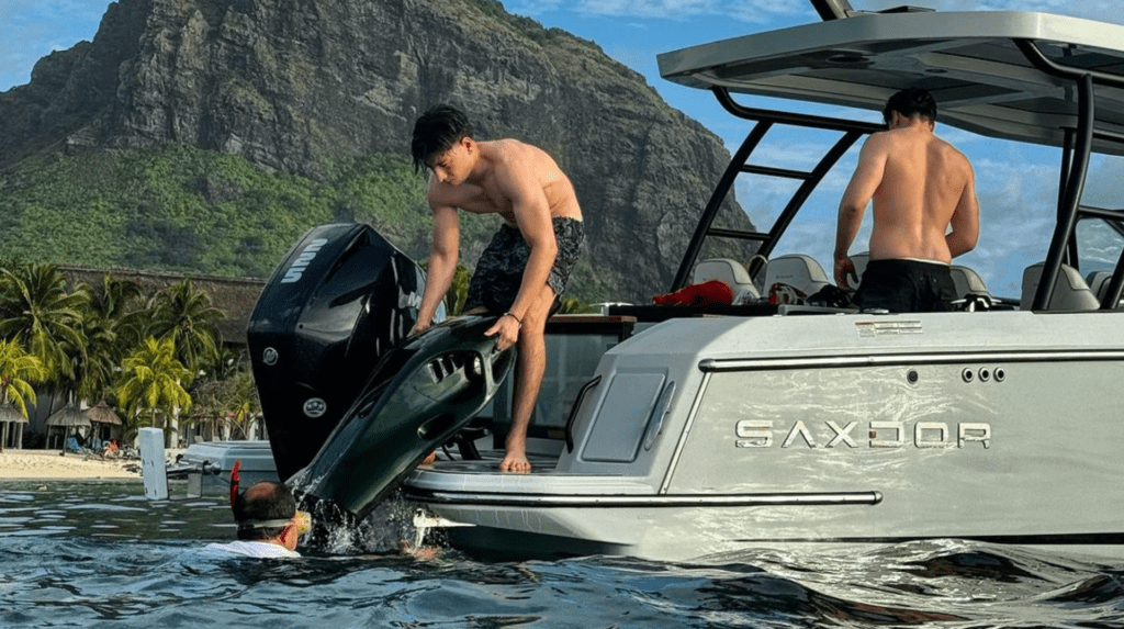 SeaNXT-Elite-Boat-Experience. Person lifting the SeaNXT Elite underwater scooter onto a boat, illustrating its lightweight design and ease of transport, with a scenic backdrop of mountains and palm trees.