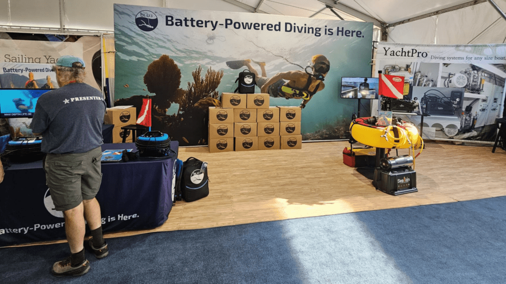 LU3 booth setup at the 2023 Annapolis Boat Show, featuring displays of BLU3 Nomad and Nomad Mini systems, a large backdrop with a diver, and boxed products stacked at the booth.