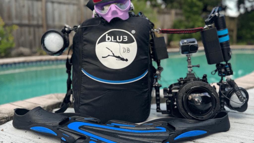 blu3-nomad-underwater-photography-gear-poolside BLU3 Nomad dive system with underwater photography gear, including fins, a professional camera setup, and a pool in the background.