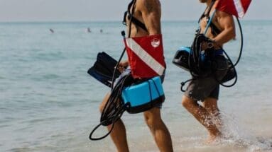 Two divers walk into water with BLU3 Nomad tankless diving system which is an alternative to snuba diving equipment.