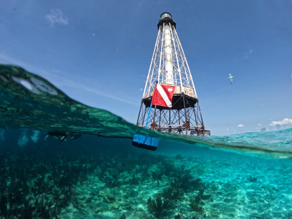 Floating BLU3 Nomad surface supplied diving system with dive flag near an offshore lighthouse in clear tropical waters.