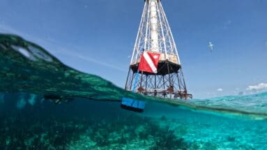 Floating BLU3 Nomad surface supplied diving system with dive flag near an offshore lighthouse in clear tropical waters.