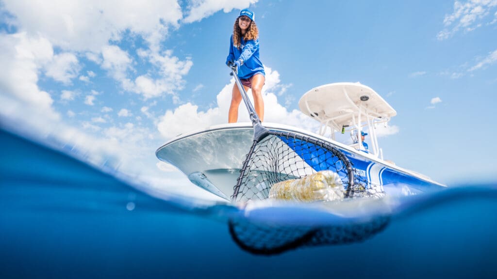 4ocean cleanup team member removing ocean plastic from the water using a net from a boat.