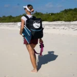 Woman walking on the beach carrying a surfboard and backpack
