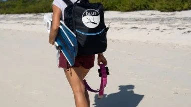 Woman walking on the beach carrying a surfboard and backpack