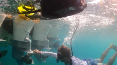 Diver inspecting underwater motors near a boat in clear blue water.