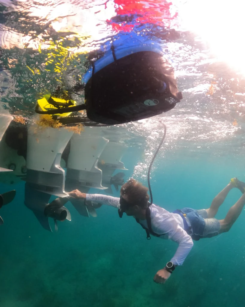 Diver inspecting underwater motors near a boat in clear blue water.