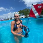 Female diver in a colorful swimsuit holding a dive flag in a pool.
