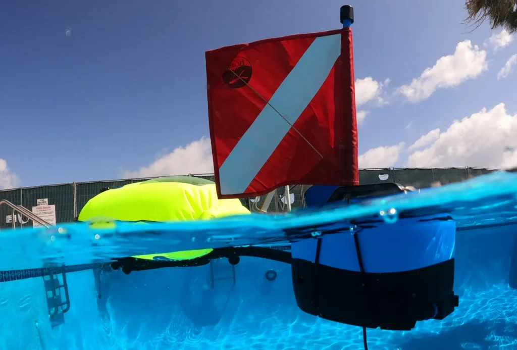 A bright red dive flag floats above water, with a buoy visible below