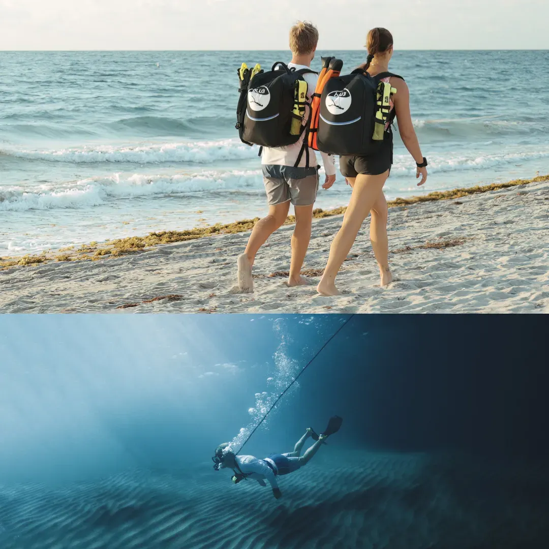 Two divers walking on a beach, carrying diving gear, with ocean waves in the background